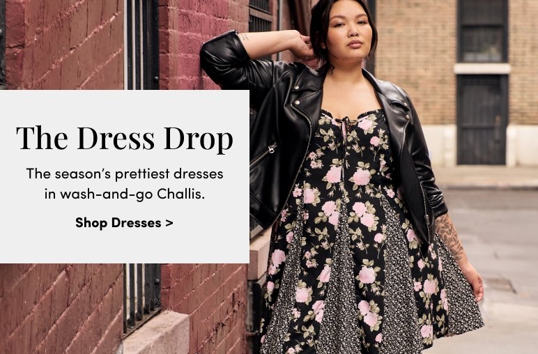 A woman in a floral dress and black leather jacket stands confidently against a brick wall. Text on the left reads: 'The Dress Drop. The season’s prettiest dresses in wash-and-go Challis. Shop Dresses > 