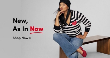 A woman modeling casual clothing, including a black and white striped sweater with a red heart detail and blue jeans, paired with red shoes. She is seated on a wooden bench, wearing a black knit hat, with a confident pose. The text on the image reads: 'New, As In Now. Shop Now >' in bold lettering.