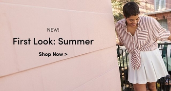 Smiling woman wearing a striped button-down shirt tied at the waist and a white skirt, standing on a balcony next to a pink wall. Text reads: NEW! First Look: Summer. Shop Now >