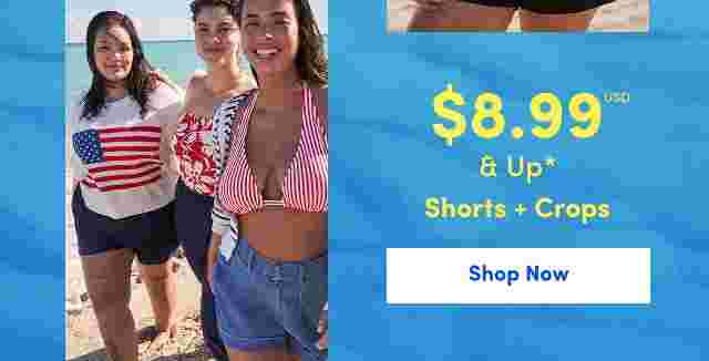 Three smiling women walking on the beach wearing summer outfits including a flag sweater, floral swimsuit, and red striped bikini top with denim shorts. Overlaid text reads 8.99 USD and up, Shorts + Crops