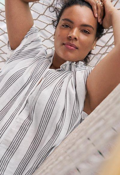 Woman lying in a hammock wearing a white blouse with vertical black stripes, looking relaxed and content.