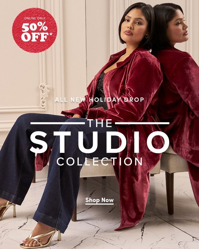 'Woman sits in a chair wearing a long dark red velvet coat over a black top and dark jeans with gold strappy heels. She faces forward while her reflection is visible in the mirror behind her. The setting has cream-colored paneled walls and white marble flooring. Large white text in the center reads ALL NEW HOLIDAY DROP THE STUDIO COLLECTION, with a white button below that reads Shop Now. In the upper left corner, a red textured circle with white text reads ONLINE ONLY 50% OFF*.'