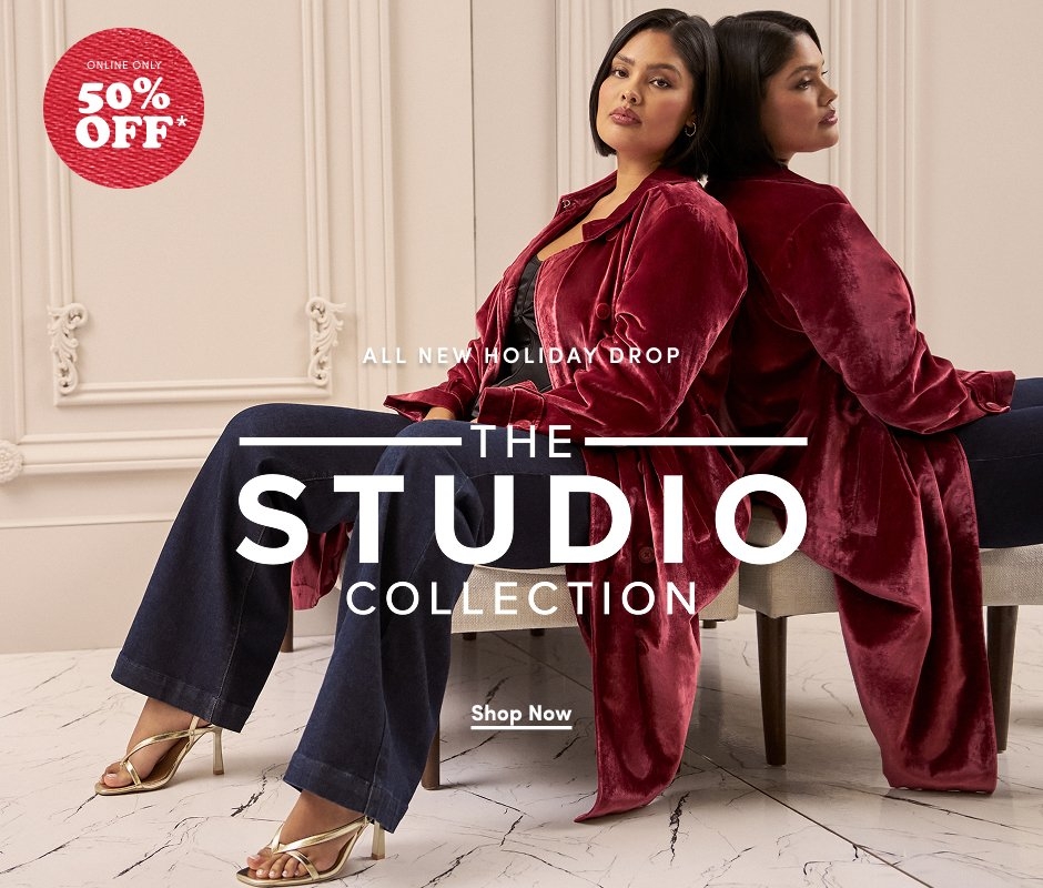 'Woman sits in a chair wearing a long dark red velvet coat over a black top and dark jeans with gold strappy heels. She faces forward while her reflection is visible in the mirror behind her. The setting has cream-colored paneled walls and white marble flooring. Large white text in the center reads ALL NEW HOLIDAY DROP THE STUDIO COLLECTION, with a white button below that reads Shop Now. In the upper left corner, a red textured circle with white text reads ONLINE ONLY 50% OFF*.'