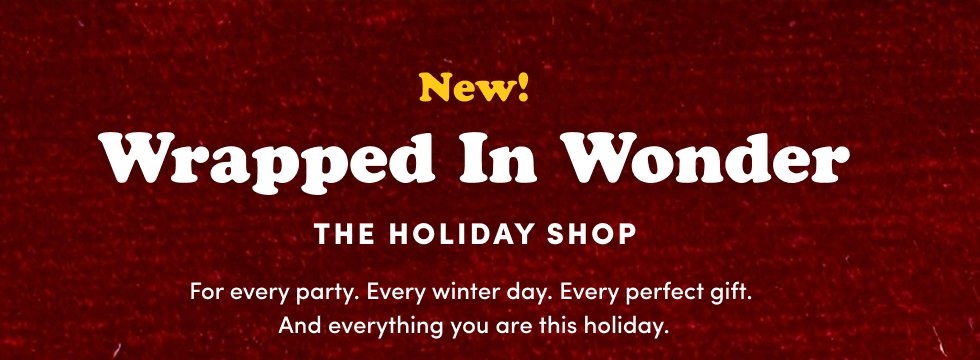 Dark red textured background with centered white and yellow text that reads 'New! Wrapped In Wonder THE HOLIDAY SHOP For every party. Every winter day. Every perfect gift. And everything you are this holiday.'