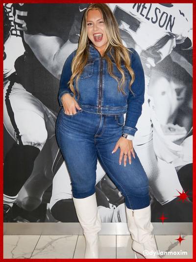 'Woman standing in front of a black and white football mural wearing a fitted dark blue denim jacket with matching high-waisted denim jeans, white knee-high boots, and a watch on her left wrist; she poses with one hand in a pocket and the other on her thigh, smiling widely with long blonde hair styled in loose waves; small red star graphics appear in the corners and the handle @dylanmoxim is printed in white near the bottom right.'
