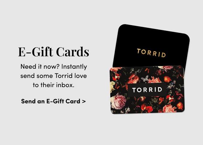 'E-Gift Cards headline in black text appears on the left above smaller text reading Need it now? Instantly send some Torrid love to their inbox. A bold black link below reads Send an E-Gift Card >. On the right, two overlapping rectangular TORRID gift cards are shown: the back card is solid black with gold TORRID text, and the front card has a black background covered in a floral pattern with red, pink, and peach flowers and centered white TORRID text.'