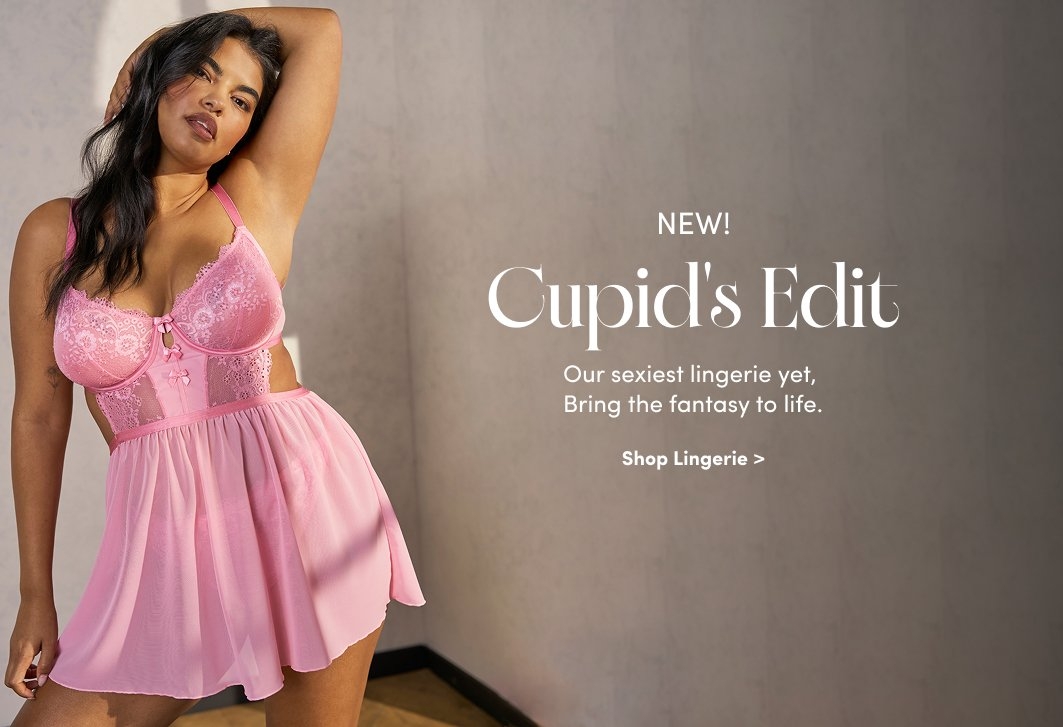 'A woman wearing a pink lace and mesh babydoll lingerie set poses with one hand in her hair against a softly lit beige wall. The lingerie has lace cups, cutouts at the sides, satin bow details at the center, and a sheer flowing skirt. White on-image text reads NEW! Cupid’s Edit. Our sexiest lingerie yet, Bring the fantasy to life. Below that, smaller white text reads Shop Lingerie >.'
