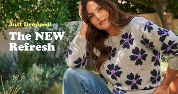 A woman sits outdoors in a garden setting wearing a light gray sweater with large purple and navy flower patterns paired with blue jeans. Text reads: “Just Dropped! The New Refresh.”