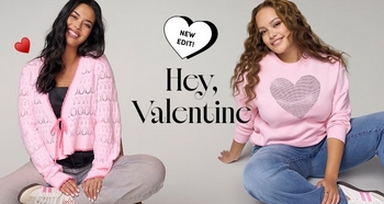 Two women sit on the floor wearing pink Valentine-themed sweaters. One wears a pink cardigan with hearts and light gray pants. The other wears a pink pullover with a large heart graphic and blue jeans. Text reads: “New Edit. Hey, Valentine.”