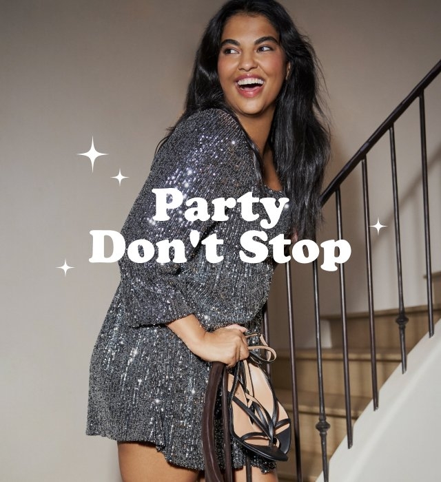 A plus-size model with long dark hair smiles and laughs while posing on a neutral-colored indoor staircase. She is wearing a shimmering silver sequined long-sleeved mini dress and holds a pair of black strappy high-heeled sandals in her left hand. Overlaid white bold text in the center reads 'Party Don't Stop' accompanied by small white four-pointed star graphics.