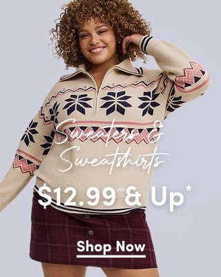 'A smiling woman with short tight curly light brown hair wears a beige quarter-zip sweater with navy and pink geometric snowflake and zigzag patterns across the chest and sleeves, ribbed cuffs with navy stripes, and a burgundy plaid mini skirt against a light gray background. White script text across the center reads Sweaters & Sweatshirts. Large white text across the lower center reads $12.99 USD & Up*. A white underlined Shop Now button appears below.'
