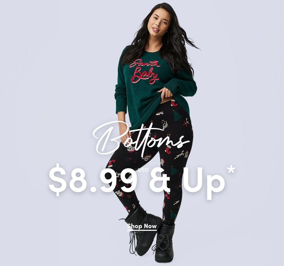 'A woman with long dark hair wears a dark green sweater with red script text reading Santa Baby and black leggings printed with holiday icons including candy canes, stockings, trees, and ornaments, paired with black lace-up boots against a light gray background. White script text across the center reads Bottoms. Large white text across the lower center reads $8.99 USD & Up*. A white underlined Shop Now button appears below.'*