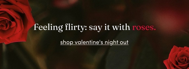 A horizontal promotional banner with a dark, moody background featuring blurred deep green and burgundy tones. A large red rose appears in the top left corner and another in the bottom right corner. Centered in the image, large white text reads 'feeling flirty: say it with' followed by the word 'roses.' in red. Below this, white underlined text reads 'shop valentine's night out'. The overall aesthetic is romantic and dramatic with rich, warm colors.