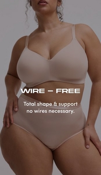 Model shown from neck to mid-thigh against a light gray background, wearing a nude pink wire-free bra with wide straps and smooth cups, paired with matching high-waisted nude pink briefs with a satin waistband. Model has curly brown hair visible at shoulders. White text overlay reads 'WIRE - FREE' with subtext below reading 'Total shape & support no wires necessary.'