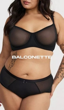 Model shown from chin to mid-thigh against a light gray background, wearing a black sheer mesh balconette bra with underwire and visible seaming, paired with black sheer mesh cheeky panties with a small bow at center front. Model has long dark wavy hair and a floral tattoo sleeve visible on left forearm. White text overlay reads 'BALCONETTE' across the midsection.