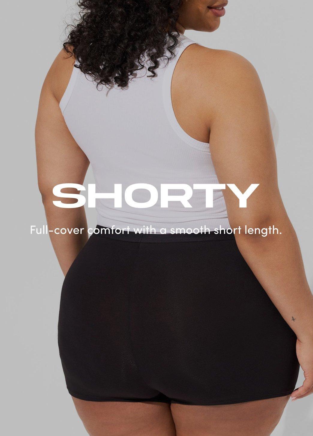 Model shown from the back wearing black shorty underwear with a white tank top against a neutral background. On image text reads Shorty. Full cover comfort with a smooth short length.