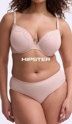 Model shown from neck to upper thighs against a light gray background, wearing a blush pink t-shirt bra with molded cups, adjustable straps, and lace trim along the neckline, paired with matching blush pink hipster panties with a smooth mid-rise waistband. Model has curly brown hair visible at the top of the frame. White text overlay reads 'HIPSTER' across the midsection.