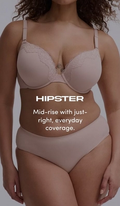 Model shown from neck to upper thighs against a light gray background, wearing a blush pink t-shirt bra with molded cups, adjustable straps, and lace trim along the neckline, paired with matching blush pink hipster panties with a smooth mid-rise waistband. Model has curly brown hair visible at the top of the frame. White text overlay reads 'HIPSTER' with subtext below reading 'Mid-rise with just-right, everyday coverage.'