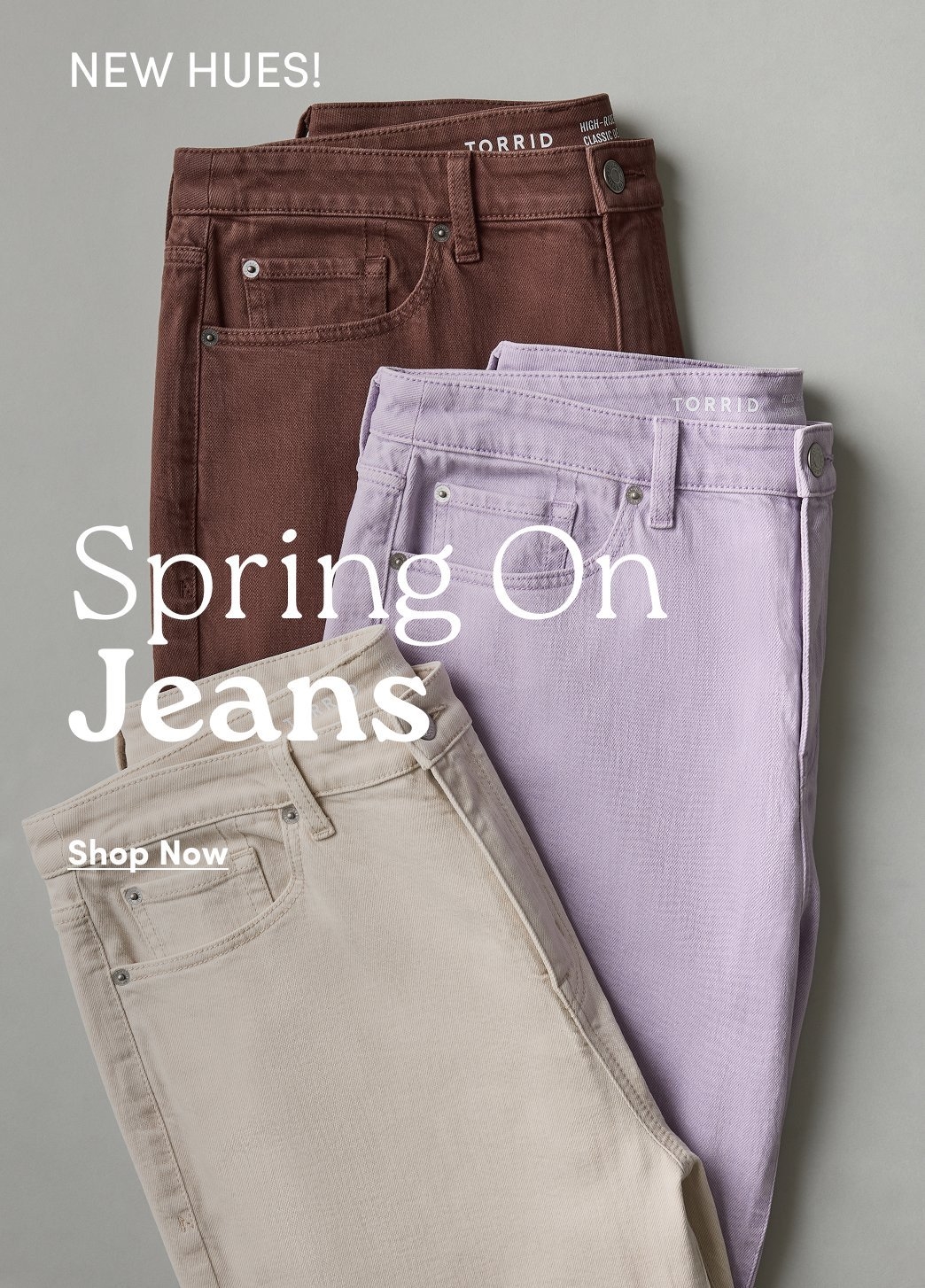 Three pairs of colored jeans folded and layered in brown, lavender, and beige against a neutral background. Text reads “NEW HUES! Spring On Jeans” and “Shop Now.”