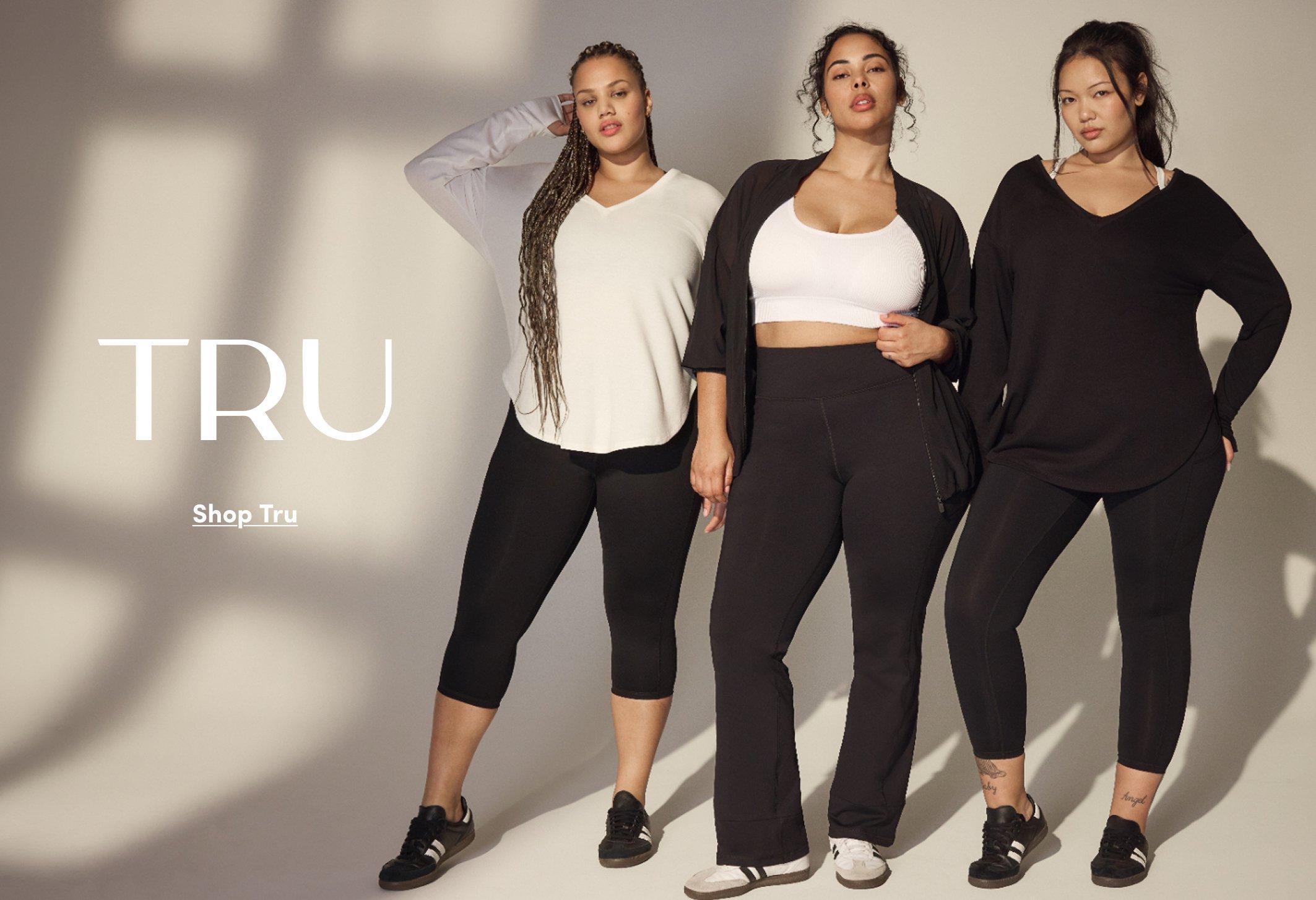 Three plus size models wearing black leggings styled with neutral tops and sneakers. One wears a white long sleeve top, one wears a white sports bra with a black open cardigan, and one wears a black oversized top. Text on the left reads “TRU” and “Shop Tru.”
