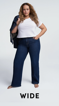 A woman with long wavy light brown hair stands barefoot against a white background with one hand in her pocket. She wears a white short-sleeve crew neck tee with a dark wash wide-leg denim jacket draped over one shoulder. Bold black text at the bottom reads 'Wide'.