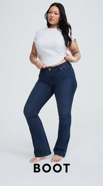 A woman with long dark hair and tattoos on both arms stands barefoot against a white background with both hands at her waist. She wears a white short-sleeve cropped crew neck tee and dark wash high-rise bootcut jeans. Bold black text at the bottom reads 'Boot'.