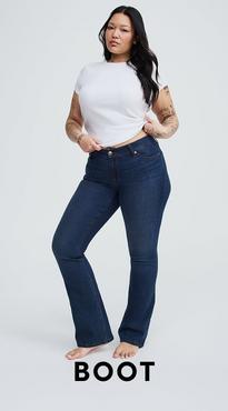 A woman with long dark hair and tattoos on both arms stands barefoot against a white background with both hands at her waist. She wears a white short-sleeve cropped crew neck tee and dark wash high-rise bootcut jeans. Bold black text at the bottom reads 'Boot'.