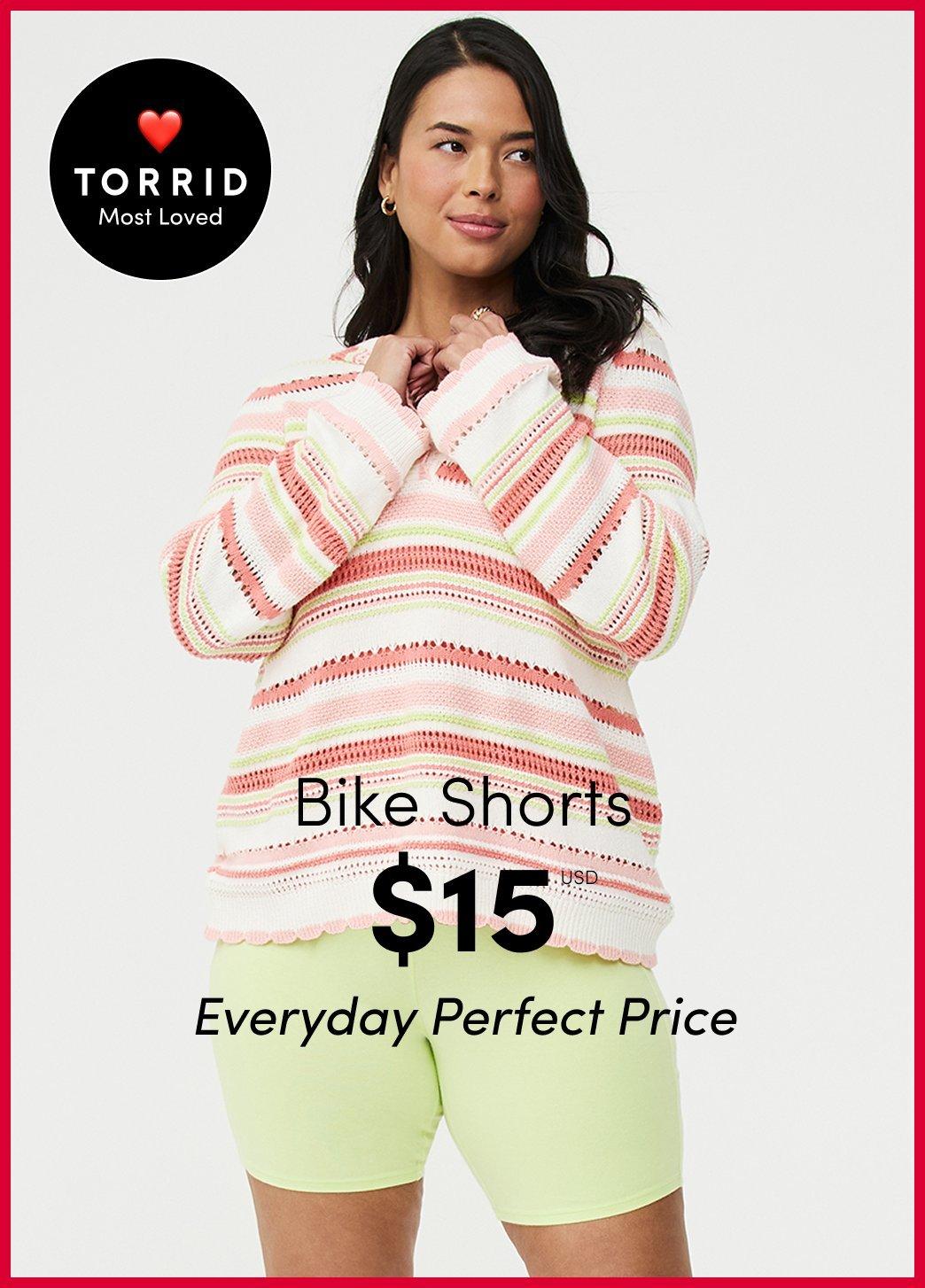 "Torrid Most Loved advertisement: Model in a pink and green striped sweater and lime green bike shorts. Text: Bike Shorts $15 USD Everyday Perfect Price."