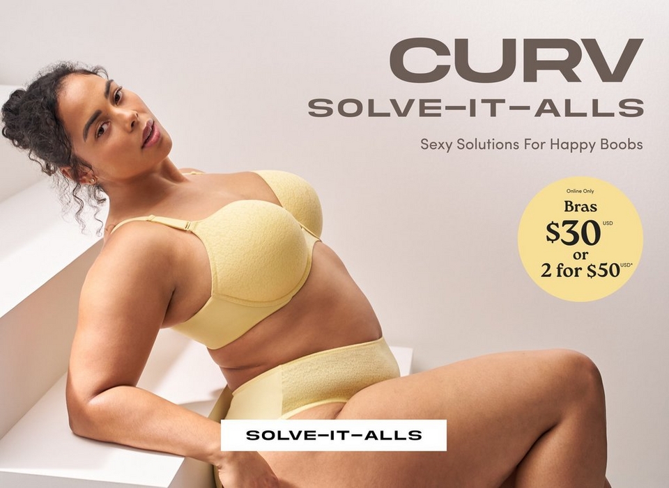 A promotional banner for 'Curv Solve-It-Alls' with the tagline 'Sexy Solutions For Happy Boobs' in dark brown text on the upper right against a light gray background. A woman with curly dark hair pulled up, small stud earrings, and a delicate necklace sits on a white geometric step or block, leaning back and looking over her shoulder. She wears a pale yellow textured strapless bra with adjustable straps and matching pale yellow high-waist briefs. A white rectangular button reading 'Solve-It-Alls' appears at the bottom center of the image.