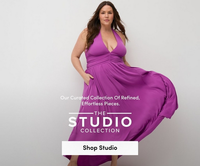A promotional banner for 'The Studio Collection' with the tagline 'Our Curated Collection Of Refined, Effortless Pieces.' and a white 'Shop Studio' button overlaid on a photo. A woman with long dark brown wavy hair and small drop earrings stands against a light gray background with one hand in a pocket, the skirt of her dress flowing to one side. She wears a bright magenta halter maxi dress with a deep V-neckline, ruched waist, and flowy skirt, paired with gold strappy heeled sandals.