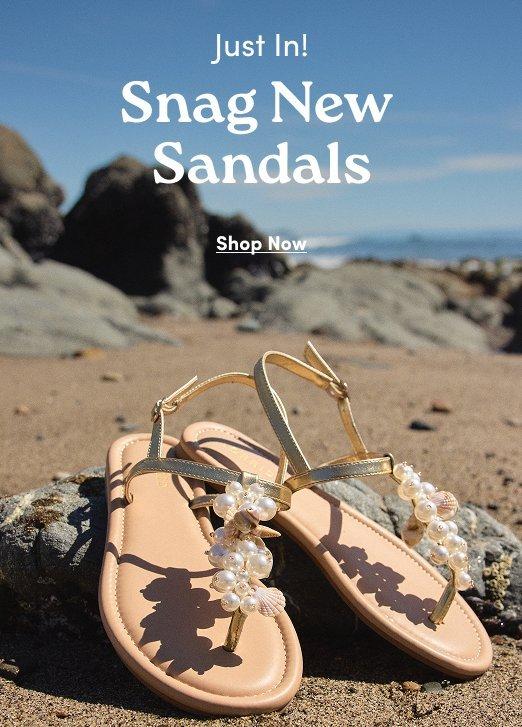 Tan sandals with pearl and shell embellishments on a beach. Text: Just In! Snag New Sandals. Shop Now.