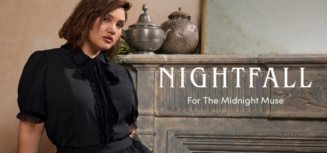 A promotional banner for 'Nightfall' with the tagline 'For The Midnight Muse' in white text on the right side, set against an ornate stone fireplace mantel with silver decorative vessels and greenery on a warm beige wall. A woman with short dark brown wavy hair, a nose ring, and defined eye makeup stands to the left looking to the side. She wears a black short-sleeve blouse with puff sleeves, a ruffled bib front, velvet bow tie at the neck, and lace cuff detail.
