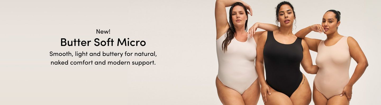 A promotional banner for 'New! Butter Soft Micro' with the tagline 'Smooth, light and buttery for natural, naked comfort and modern support.' in black text on a warm off-white background. Three women stand close together against a light gray background. The woman on the left has long dark hair with one arm raised overhead and wears a white smooth seamless scoop-neck thong bodysuit. The woman in the center has dark curly hair pulled up and one hand raised near her chin, wearing a black smooth seamless scoop-neck thong bodysuit. The woman on the right has dark hair in a bun and one hand raised near her chin, wearing a blush pink smooth seamless scoop-neck thong bodysuit with a small tattoo visible on her leg.