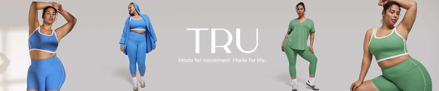 A promotional banner for 'TRU' with the tagline 'Made for movement. Made for life.' in white text centered against a light gray background. Four photos show two women in coordinated activewear sets. On the far left, a woman with dark hair pulled up and one arm raised overhead wears a cornflower blue ribbed sports bra crop top with white trim and matching blue ribbed biker shorts with white piping. Next to her, a taller woman with dark hair and hoop earrings wears a matching bright blue set consisting of a sports bra, high-waist cropped leggings, and an oversized zip-up hoodie, with white ankle socks and chunky sneakers. On the right side, a woman with dark hair in a bun wears a sage green V-neck oversized short-sleeve top with matching sage green cropped leggings, white ankle socks, and white sneakers with a dark sole. On the far right, the same woman is shown in a closer crop wearing a sage green ribbed sports bra crop top with white trim and matching sage green ribbed biker shorts with white piping, one arm raised overhead.