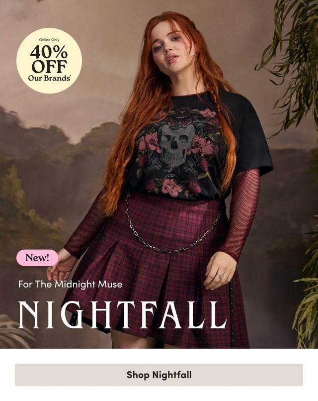 'Promotional banner for Torrid Nightfall collection against a dark, moody painted backdrop depicting a misty jungle landscape with trees, tropical foliage, and a cloudy sky in muted brown and green tones. Hanging green vines are visible on the right edge. A plus-size woman with long wavy red hair and light skin stands in the center of the image, looking slightly downward. She is wearing a black graphic t-shirt featuring a skull and floral rose design, layered over a long-sleeve black fishnet top, paired with a dark burgundy and black plaid pleated mini skirt with a silver chain belt and black studded strap detail. She wears rings on both hands. In the upper left corner is a pale yellow circle badge with dark text reading 'Online Only 40% OFF Our Brands' with an asterisk. On the lower left, a small pink rounded badge reads 'New!' above smaller white text reading 'For The Midnight Muse', followed by large white serif text reading 'NIGHTFALL'. At the bottom is a light gray rectangular button with bold dark text reading 'Shop Nightfall'.'