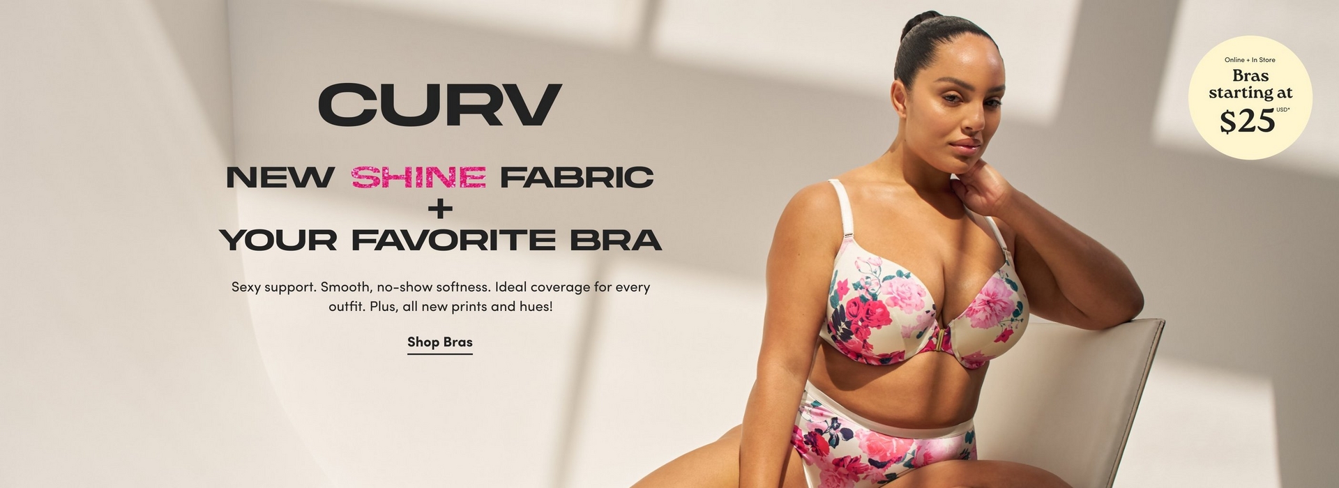 'Promotional banner for Torrid CURV on a light beige background with soft angular shadow shapes. A plus-size woman with medium skin tone and dark hair pulled back is seated on a light-colored chair, posing with one hand resting near her face. She is wearing a cream-colored bra and high-waist briefs with a pink, red, and teal floral print, and a gold front clasp detail on the bra. On the left, large bold dark text reads 'CURV' above bold dark text reading 'NEW' with 'SHINE' in bold pink, followed by 'FABRIC + YOUR FAVORITE BRA'. Smaller dark text below reads 'Sexy support. Smooth, no-show softness. Ideal coverage for every outfit. Plus, all new prints and hues!' Below that, bold dark underlined text reads 'Shop Bras'. In the upper right corner is a pale yellow circle badge with dark text reading 'Online + In Store Bras starting at $25 USD' with an asterisk.'