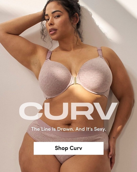 'Promotional banner for Torrid CURV against a warm beige background with soft light and shadow. A plus-size woman with medium skin tone and dark hair pulled up in a loose bun leans against a wall with one hand raised behind her head, looking to the side. She is wearing a dusty mauve heathered t-shirt bra with a gold front clasp detail and matching high-waist bikini briefs, with a small heart tattoo visible on her hip. Large bold white text overlaid on the lower portion reads 'CURV' with smaller white text above reading 'The Line Is Drawn. And It's Sexy.' At the bottom is a white rectangular button with bold dark text reading 'Shop Curv'.'