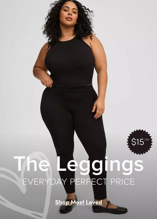 A full-length promotional image of a woman with curly dark hair wearing a matching black athletic set consisting of a high-neck halter tank top and high-waisted leggings. She is posing against a light gray gradient background and wearing black ballet flats with ribbon ties.