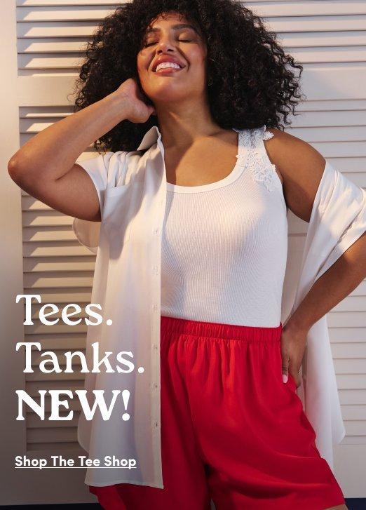 'Promotional banner for Torrid against a background of white wooden shutters. A plus-size woman with medium skin tone and voluminous dark curly hair smiles broadly with one hand raised near her face. She is wearing a white sleeveless tank top with lace trim at the shoulders, layered under a white short-sleeve open button-front shirt, paired with bright red wide-leg shorts with an elastic waist. Overlaid in the lower left in white serif text is 'Tees. Tanks.' followed by bold white text reading 'NEW!' Below that, small dark underlined text reads 'Shop The Tee Shop'.'