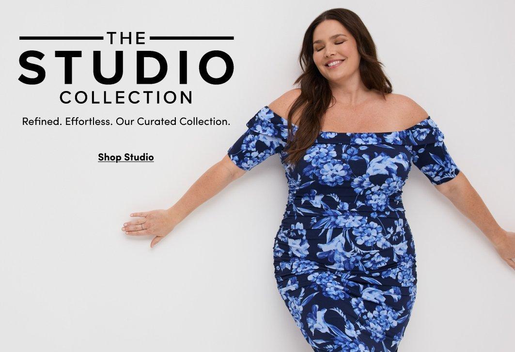 'Promotional banner for Torrid featuring Retro Chic, set in an elegant vintage-styled room with white paneled walls, a wall-mounted brass lamp, and a pink floral upholstered settee. A plus-size woman with light skin tone and long wavy blonde hair with bangs smiles broadly, holding out the skirt of her dress. She is wearing a light blue polka dot fit-and-flare midi dress with flutter sleeves, a teal satin bow at the collar, and a matching teal belt at the waist. A small dark teal rounded badge reads 'NEW DROP!' above large white cursive script text reading 'Retro Chic' with smaller white text below reading 'Vintage Vibes That Love Curves.' Below that, small dark underlined text reads 'Shop Retro Chic'.'