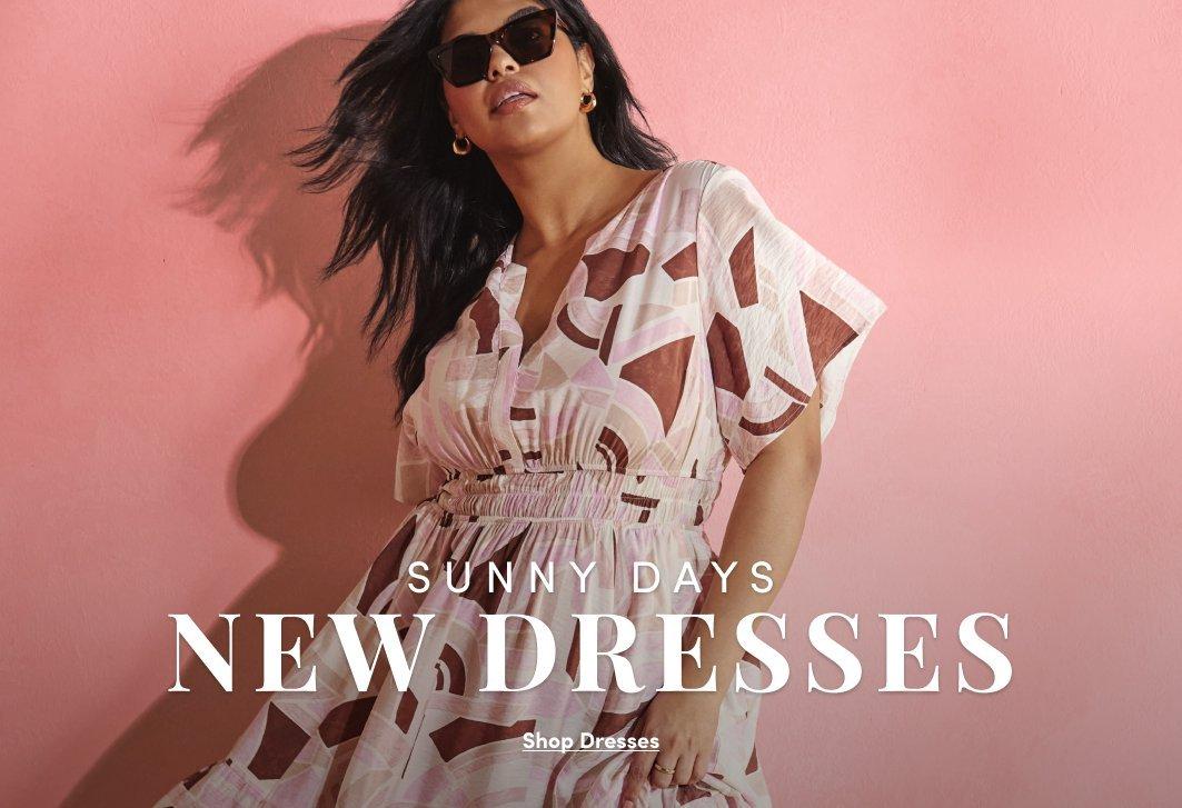 'Promotional banner for Torrid against a solid pink background. A plus-size woman with medium skin tone and long dark hair poses with her hair and skirt appearing to move as if in a breeze, wearing dark square-frame sunglasses and a cream, pink, and brown abstract geometric print wrap midi dress with flutter sleeves and a smocked waist. Overlaid in the center, small white text reads 'SUNNY DAYS' above large bold white text reading 'NEW DRESSES'. Below that, small white underlined text reads 'Shop Dresses'.'