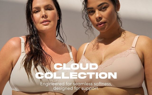 'A close cropped promotional banner for the Cloud Collection featuring two plus-size women with long dark wet hair posed closely together against a soft warm beige background with gentle light and shadow. The woman on the left wears a cream wireless bra with subtle lace floral embroidery detailing and wide adjustable straps. The woman on the right wears a blush pink bra with a smooth molded cup and a delicate scalloped lace trim across the upper cup, with visible adjustable straps. Bold white text in the lower center reads 'CLOUD COLLECTION' with smaller white text below reading 'Engineered for seamless softness, designed for support.''