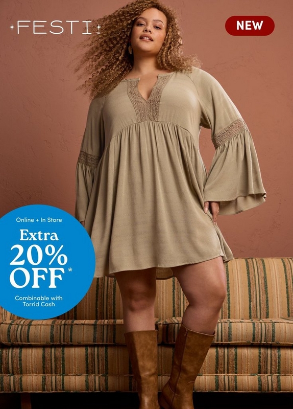 'A plus-size woman with long voluminous curly auburn hair poses standing on a striped green and tan upholstered sofa against a warm terracotta brown wall. She wears small gold earrings and a sage green babydoll mini dress with a V-neckline featuring lace trim detailing, an empire waist with gathered skirt, long bell sleeves with lace trim banding at the elbow, and a relaxed flowy silhouette. She is paired with tall tan leather knee-high boots. White text in the upper left reads '+FESTI+ TM' and a dark red rounded badge in the upper right reads 'NEW' in white text. A bright blue circle badge in the lower left contains white text reading 'Online + In Store' above 'Extra' and large text reading '20% OFF*' with smaller text below reading 'Combinable with Torrid Cash'.'