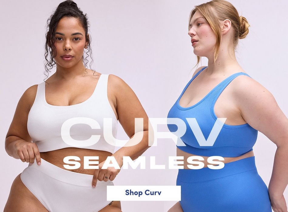 'A promotional banner for Curv Seamless featuring two plus-size women against a soft lavender-gray background. On the left, a woman with dark curly hair pulled back looks directly at the camera wearing a white ribbed seamless scoop-neck sports bra crop top with matching high-waist seamless bikini briefs. On the right, a woman with strawberry blonde hair in a loose bun looks to the side wearing a periwinkle blue ribbed seamless scoop-neck racerback sports bra crop top with matching high-waist seamless shorts. Large semi-transparent text in the center reads 'CURV' above bold white text reading 'SEAMLESS'. A white rectangle button at the bottom center contains dark text reading 'Shop Curv'.'
