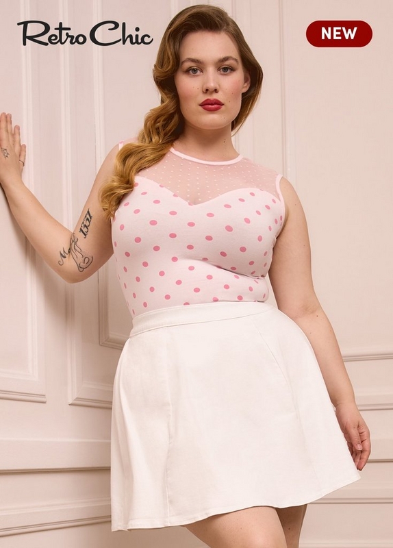 'A plus-size woman with auburn hair styled in a vintage side-swept wave and bold red lipstick leans one hand against a cream paneled wall. She has tattoos on her left forearm. She wears a light pink sleeveless top with a sheer polka dot mesh yoke at the neckline and a sweetheart-shaped opaque bodice with larger hot pink polka dots, paired with a white high-waist A-line mini skirt with a clean tailored silhouette. White script text in the upper left reads 'Retro Chic' and a dark red rounded badge in the upper right reads 'NEW' in white text.'