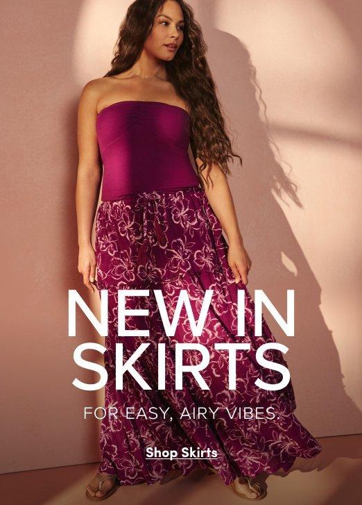 A woman with long wavy hair models a magenta tube top and a matching floral tiered maxi skirt against a pink-toned wall. Large white text overlaid on the image reads "NEW IN SKIRTS," followed by the tagline "FOR EASY, AIRY VIBES." A "Shop Skirts" link is located at the bottom.