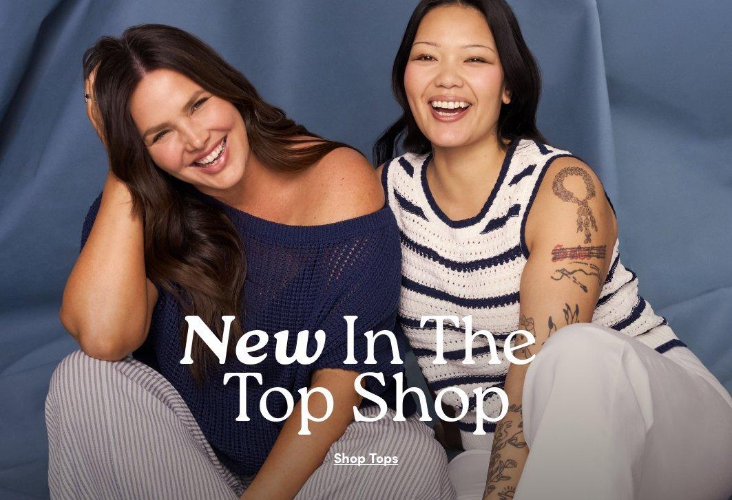 A promotional image featuring two smiling women posed against a draped blue fabric background. The woman on the left has long brown hair and is wearing a textured, off-the-shoulder navy blue sweater. The woman on the right has dark hair, is laughing, and wears a white sleeveless knit top with horizontal navy stripes. Large, elegant serif text in the foreground says "New In The Top Shop," followed by a call-to-action button that says "Shop Tops."