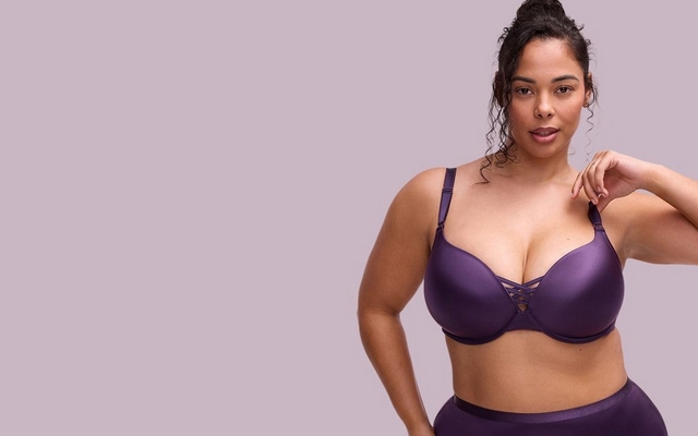 Mobile promotional banner for the Shine Collection featuring a model against a light lavender background. She is wearing a deep purple satin bra with a strappy crisscross detail at the center gore and matching high-waisted panties.