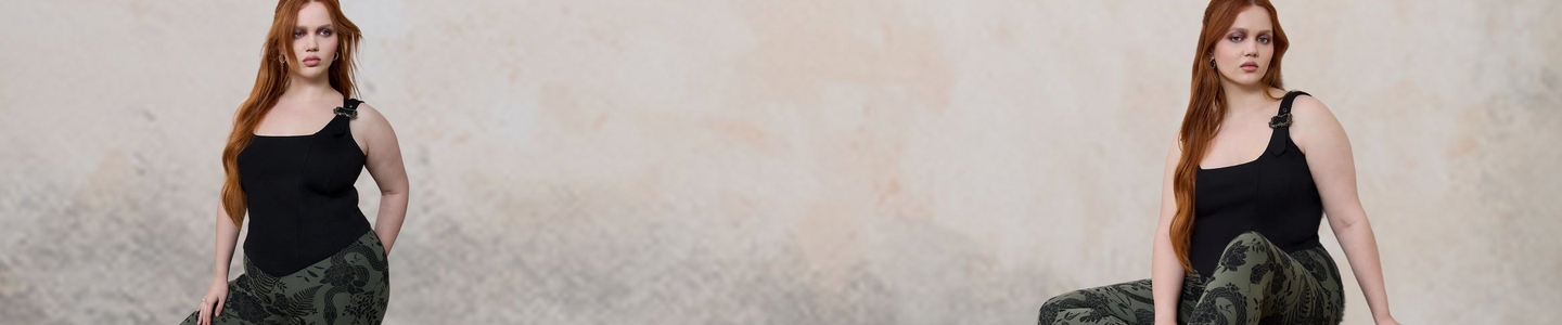 'A wide promotional banner featuring the same plus-size woman with long straight auburn hair shown from two angles against a weathered cream and beige textured wall with a graveled ground. She wears smoky eye makeup, small drop earrings, a fitted black square-neck tank top with a decorative black floral applique detail on one strap, and olive green leggings with an all-over black botanical and peacock jacquard print. On the left she faces slightly forward, and on the right she is seated and angled toward the camera.'