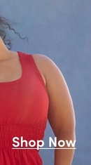 A close-up cropped vertical image of a woman wearing a red sleeveless dress with a smocked waistband, leaning against a weathered wooden post with a blue wall in the background. Only her torso, one raised arm, and part of her face with dark curly hair are visible. White underlined text at the bottom reads 'Shop Now'.